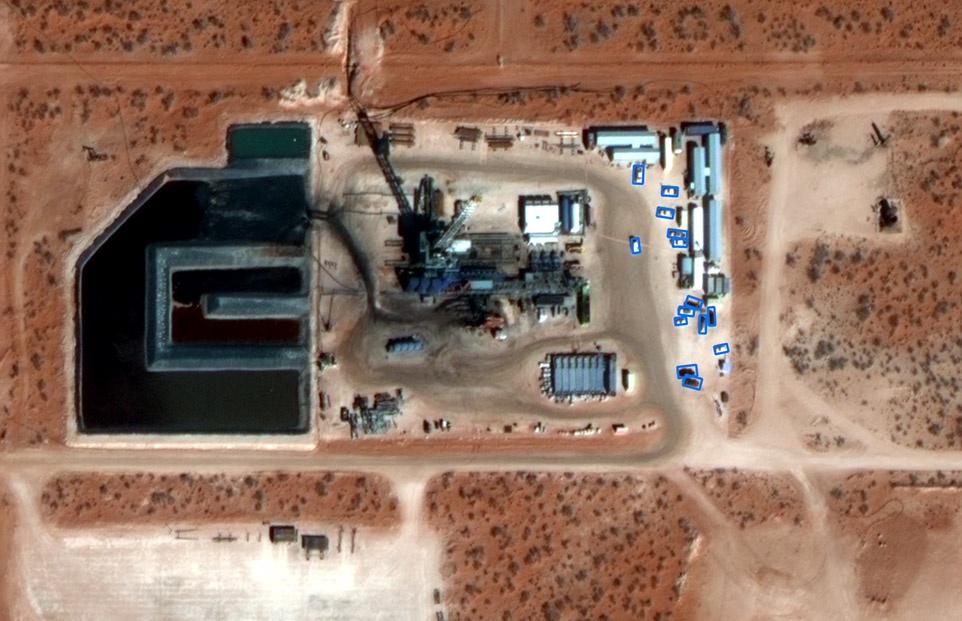 Aerial view of an active onshore oil and gas well site with equipment, storage ponds, and surrounding desert terrain, illustrating real-time monitoring capabilities.
