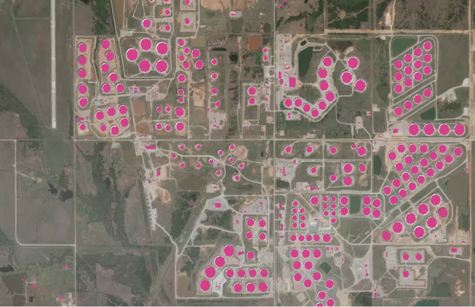 Aerial view of an active onshore oil and gas well site with equipment, storage ponds, and surrounding desert terrain, illustrating real-time monitoring capabilities.