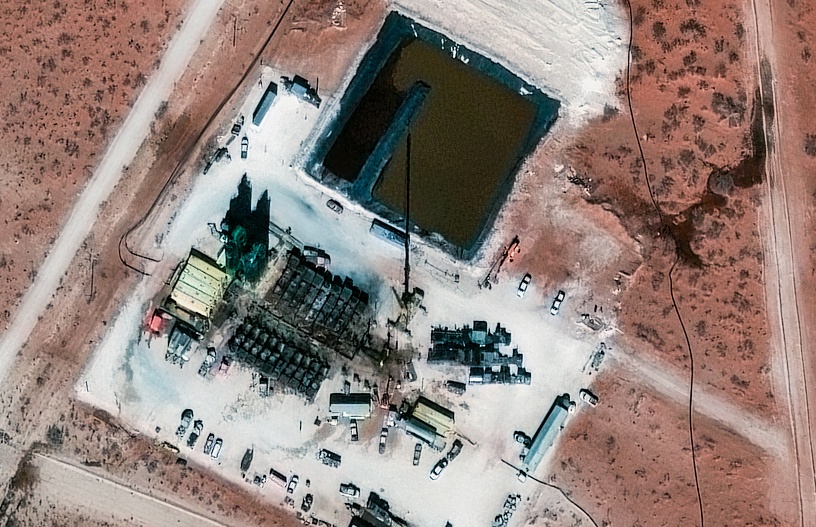 Aerial view of an oil and gas production site with equipment, storage ponds, and surrounding arid landscape, illustrating operational optimization.
